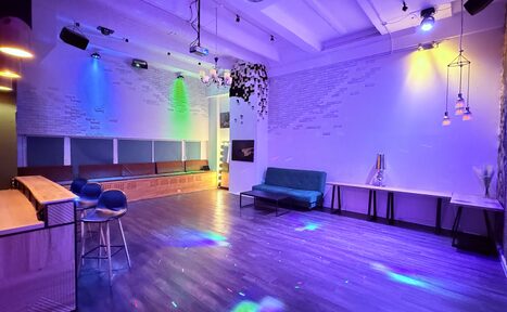 Арендовать Barshowplace (БарШоуПлейс). Лофт для вечеринок с коктейльным баром . Просторное помещение с барной стойкой и высокими стульями, диванами вдоль стены, столами и скамьями. Освещение разноцветное, свет от прожекторов. Потолок белый, стены с узором из белых и светлых кирпичей. Пол темный, деревянный.