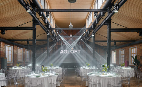 Арендовать AG Loft. Urban (АГ Лофт. Урбан). Просторный лофт с раритетным автомобилем. Лофт-пространство с высокими деревянными потолками и кирпичными стенами. Размещены круглые столы с белыми скатертями и прозрачными стульями. Простор освещается большими окнами и подвесными светильниками. На задней стене надпись «AGLOFT». Помещение в хорошем состоянии.