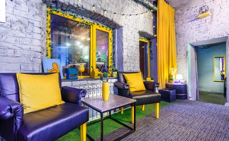 Арендовать Уютный лофт с яркими акцентами с летней верандой. Лаунж-зона с каменными стенами, двумя желтыми окнами и яркими шторами. Две кожаные синие кресла с желтыми подушками, столик с вазой. На полу ковровое покрытие и декоративный искусственный газон. Настольные лампы и подсветка.