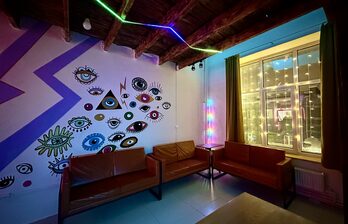 Приглушённый свет. Диваны. Стена с рисунками. Окно со светящейся гирляндой