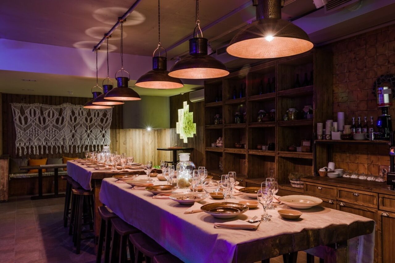 Арендовать Нора. Оборудованный зал. Затемнённое освещение. Столы с сервировкой. Подвесные лампы