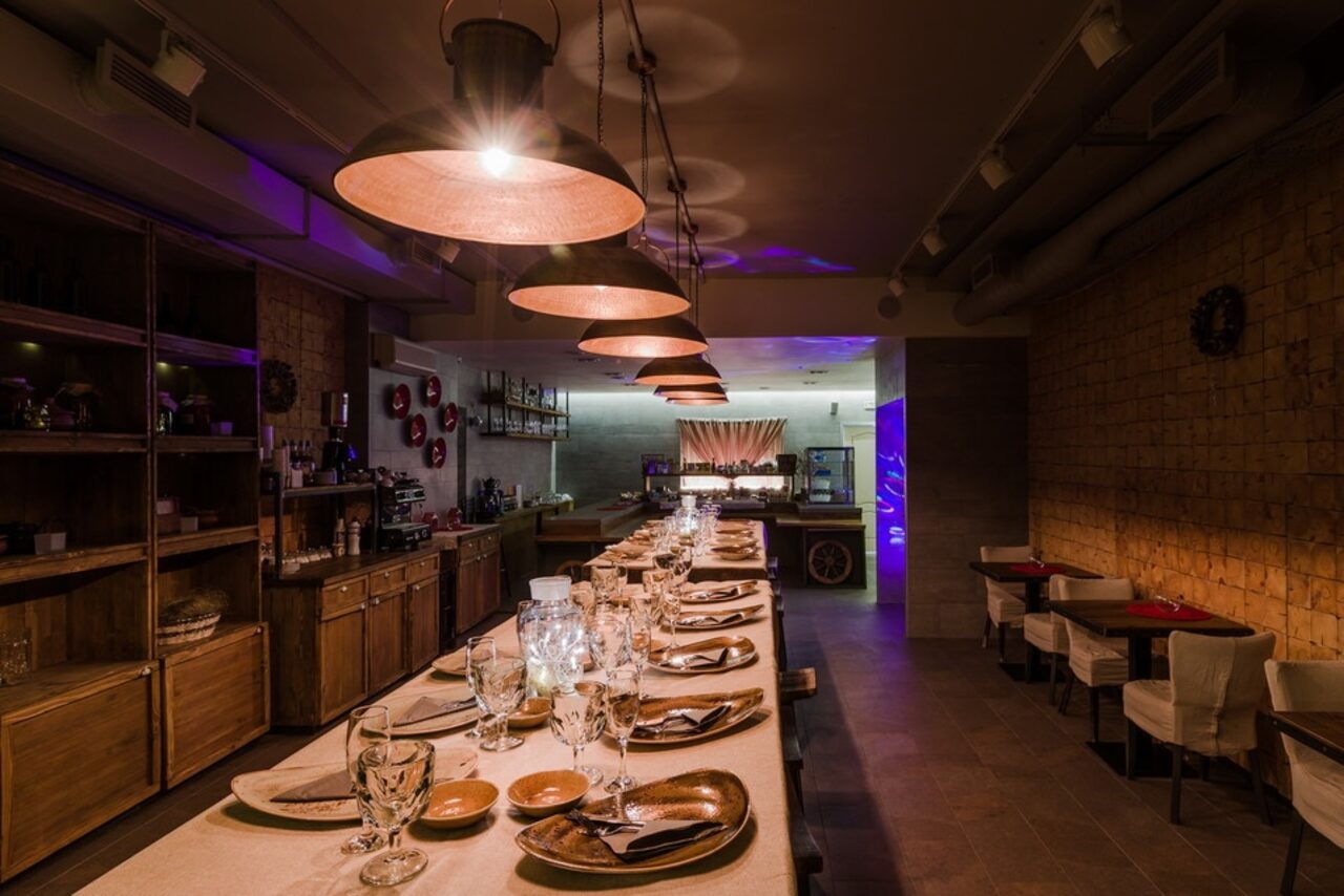 Арендовать Нора. Оборудованный зал. Затемнённое освещение. Столы с сервировкой. Подвесные лампы. Небольшие столики "на двоих"