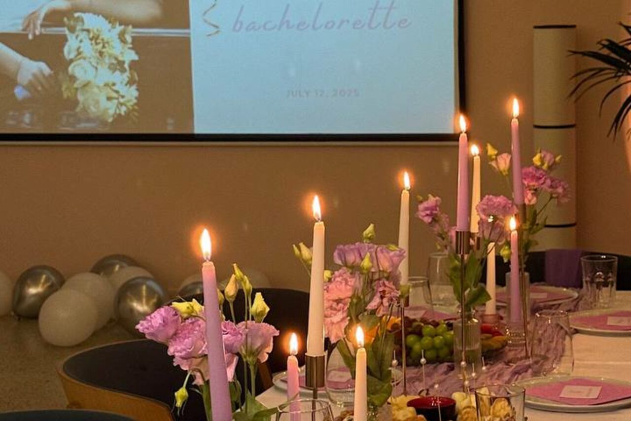 Арендовать Стилизованный лофт в сине-розовых оттенках. Пространство для мероприятий с декорированным столом; на столе розовые и белые свечи, цветы, стеклянные бокалы, блюда с фруктами; рядом экран с надписью «Bachelorette» и датой; сзади серебристые и белые шары; стены нейтрального цвета.