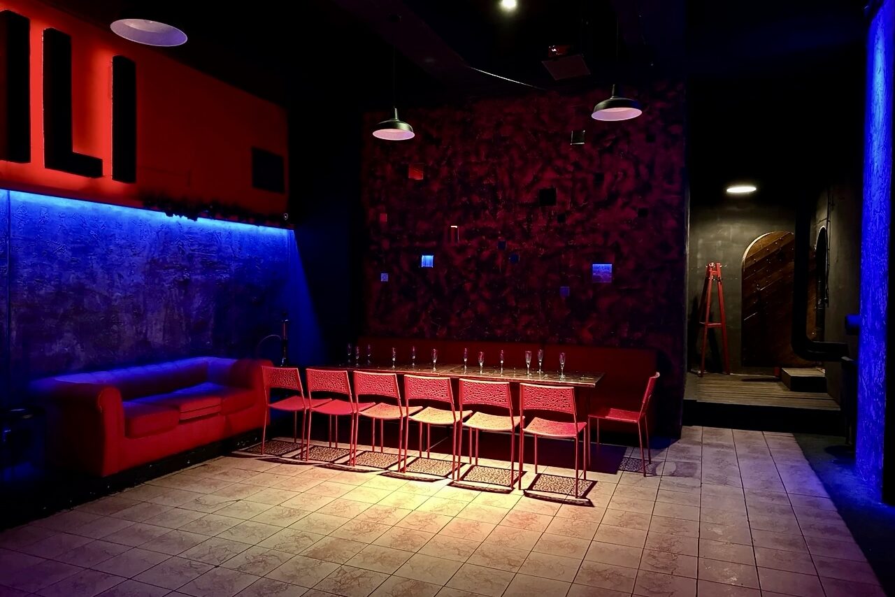 Арендовать Лофт-клуб с большим танцполом. Накрытый посудой стол. Диван. Подсвеченные символы на стене