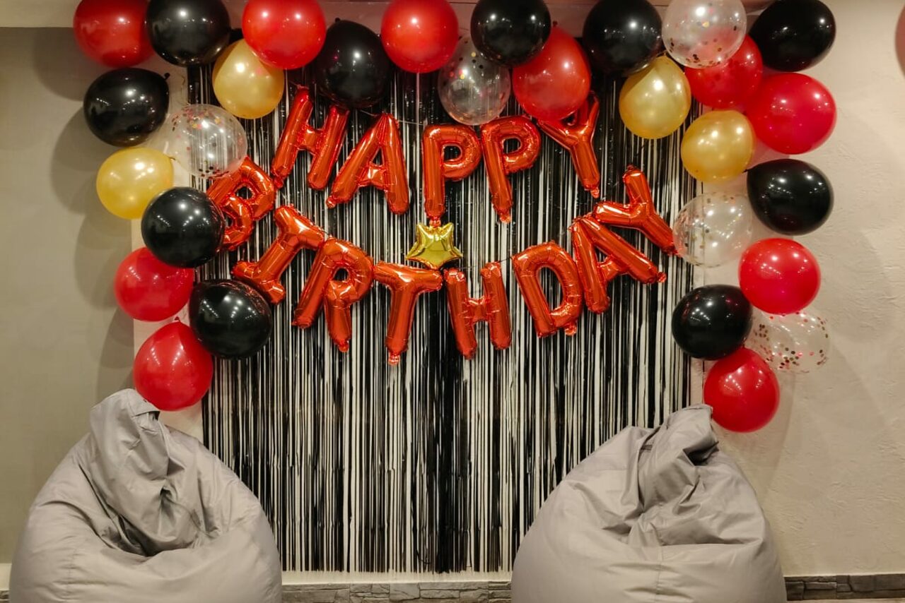 Арендовать Уютный лофт с меловой стеной. Пространство для мероприятий с декоративной аркой из воздушных шаров красного, черного, золотого и прозрачного цветов. Надпись "Happy Birthday" из шаров. Два серых кресла-мешка. Штора с полосками. Светлые стены.