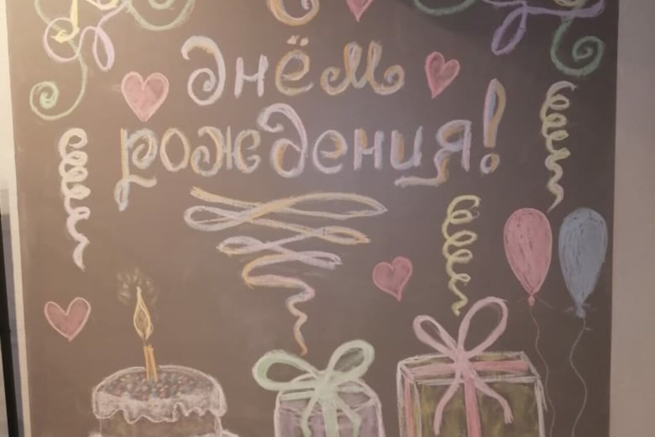 Арендовать Уютный лофт с меловой стеной. Настенная доска с надписью «С днём рождения!» и рисунками мелом: торт со свечой, подарки с бантами, воздушные шары и спирали. Цвета: розовый, зелёный, жёлтый.