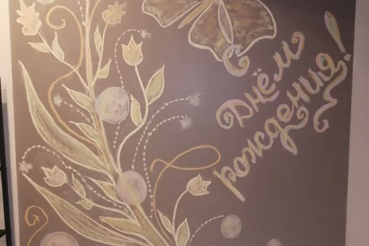 Арендовать Уютный лофт с меловой стеной. Настенная роспись с изображением цветочных мотивов и крупной бабочки на сером фоне. Рядом надпись: "С днём рождения!". Цвета росписи нежные, с преобладанием пастельных оттенков.