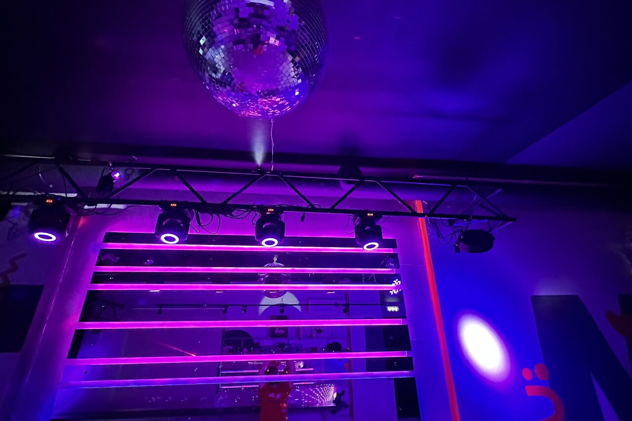 Арендовать Музыкальный лофт на Тульской. Серые диваны с красными подуками, барная стойка, праздничная достветка фиолетовым и желтым цветом.