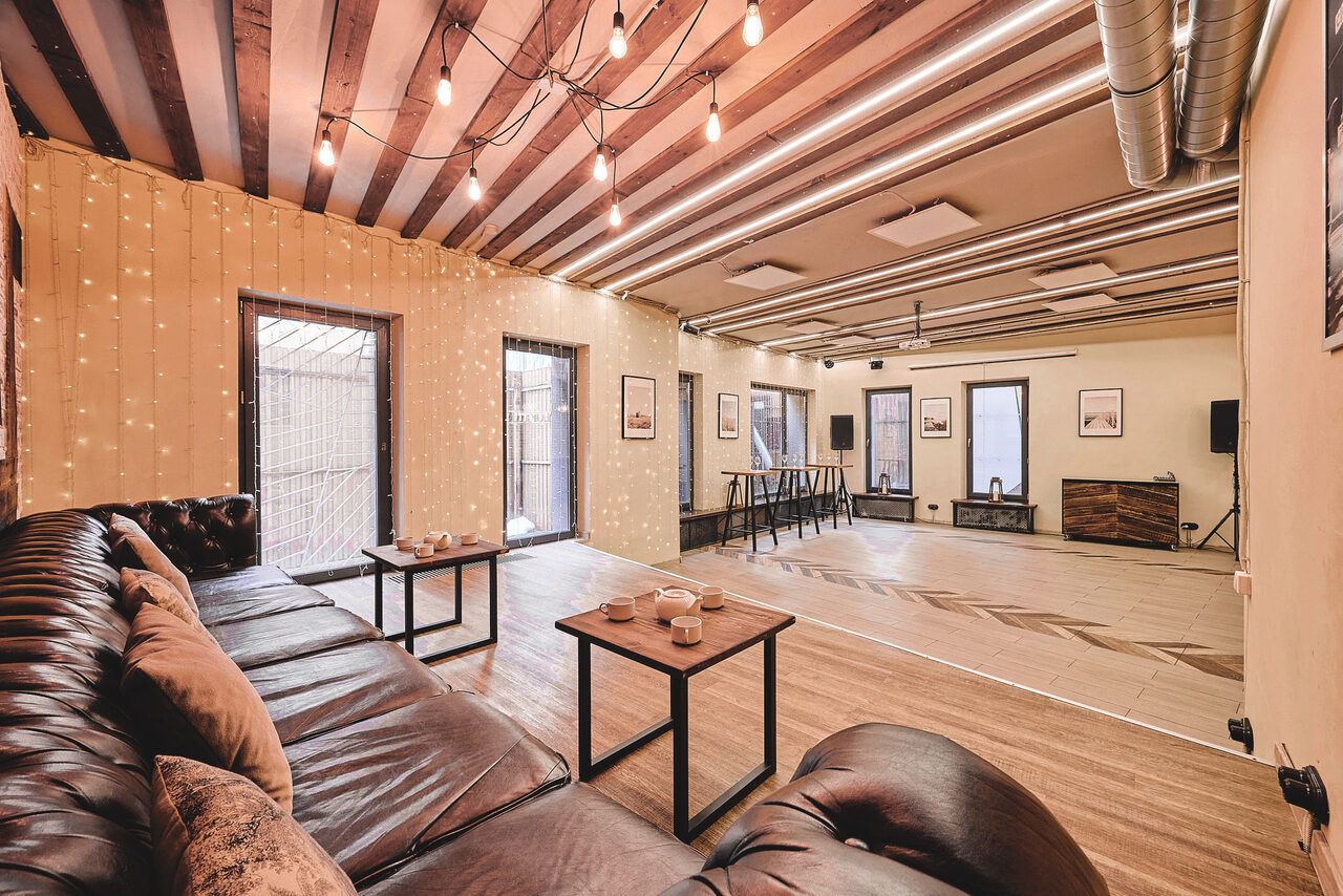 Арендовать Loft Lodge 6. Просторное помещение с кирпичными и деревянными элементами. Просторная зона отдыха с коричневым кожаным диваном и деревянными столиками. Потолок украшен подвесными лампами. Естественное освещение через большие окна. Светлые стены, деревянный пол, наличие музыкальной системы.