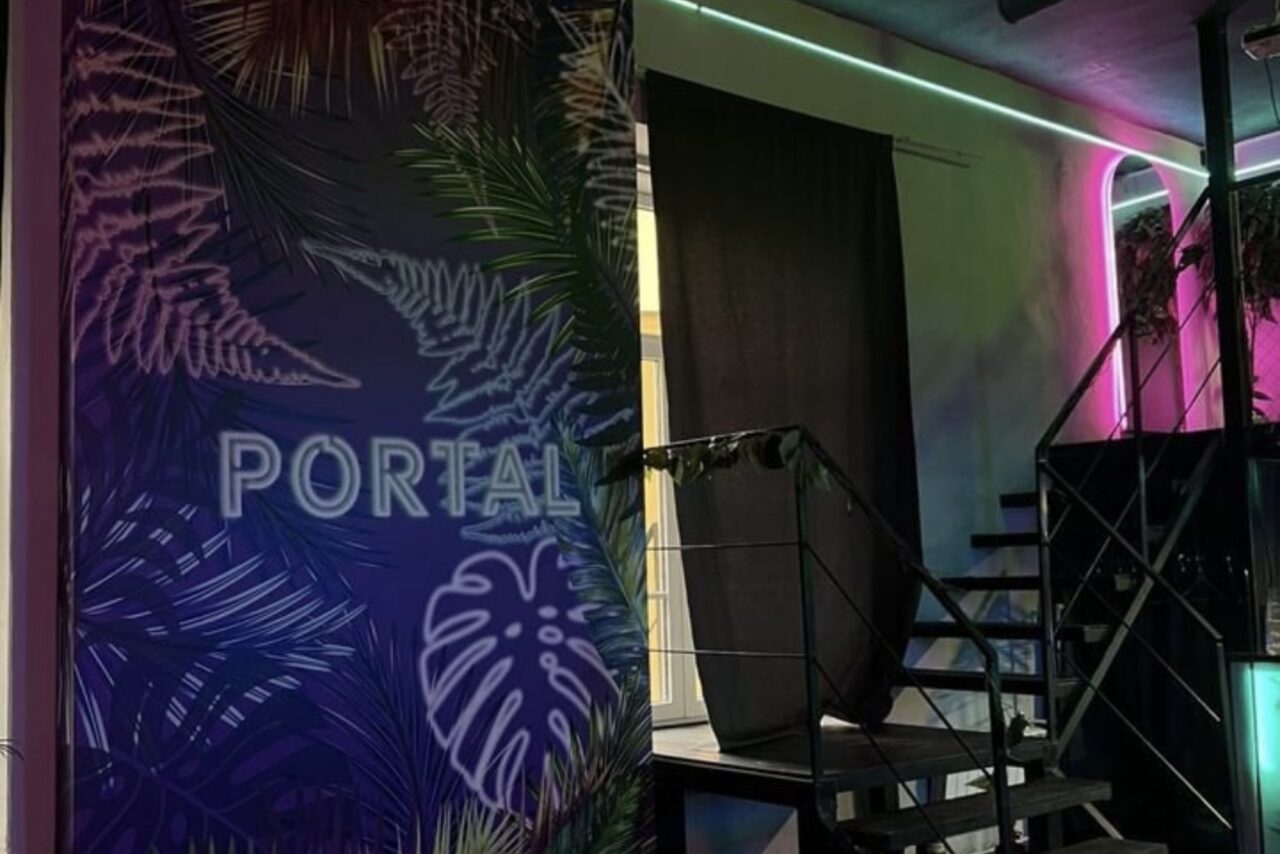 Арендовать The Portal (Портал). Тёмный неоновый лофт. Лофт, металлическая лестница, неоновая подсветка розовых и зеленых оттенков, цветочная стена с надписью "PORTAL", темная штора.