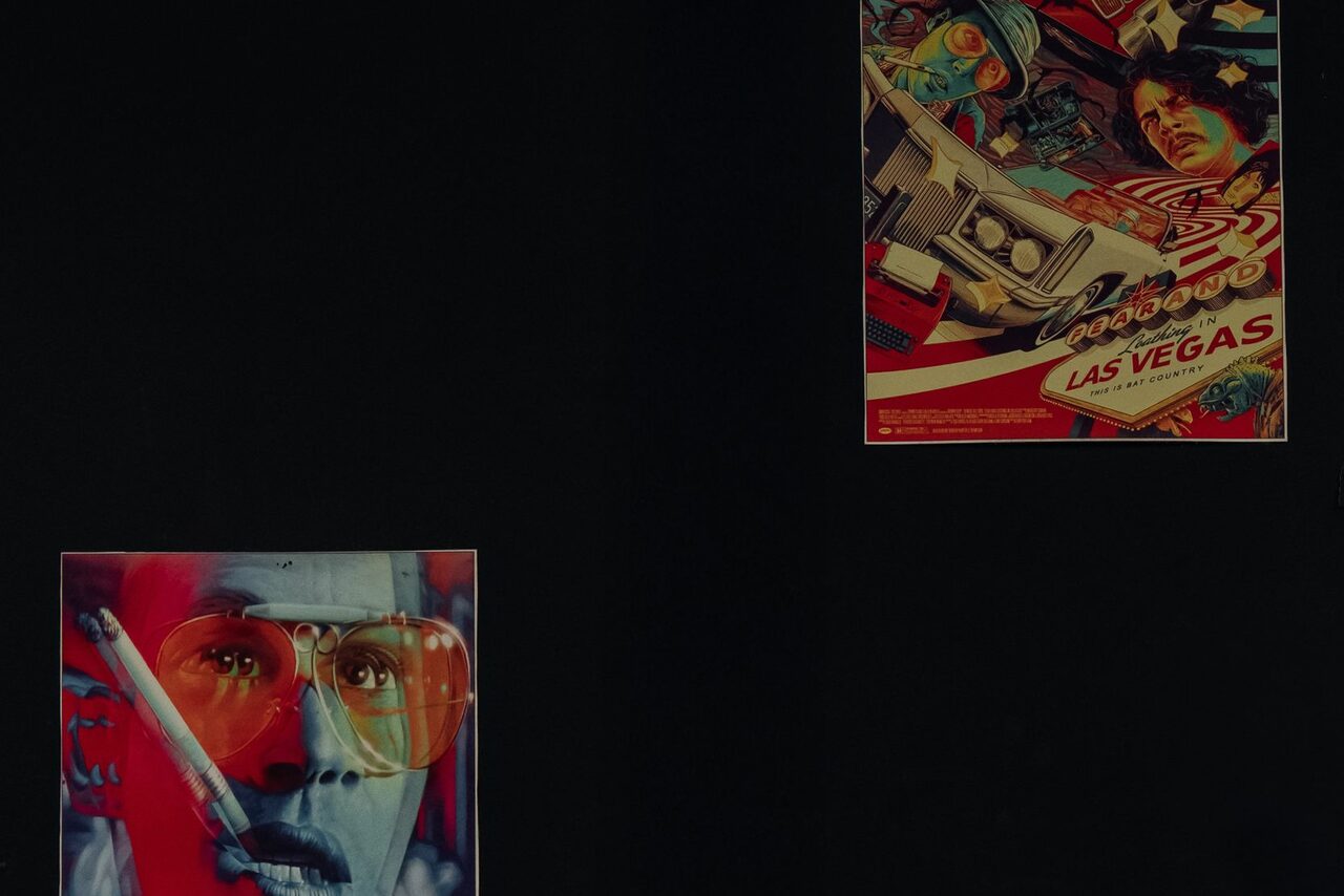 Арендовать Зал Лас-вегас. Лофт-зал в американском стиле . Черная стена с двумя постерами. Левый постер: лицо в красочных тонах с сигаретой, текст отсутствует. Правый постер: художественное изображение с автомобилем, людьми и текстом "Las Vegas".