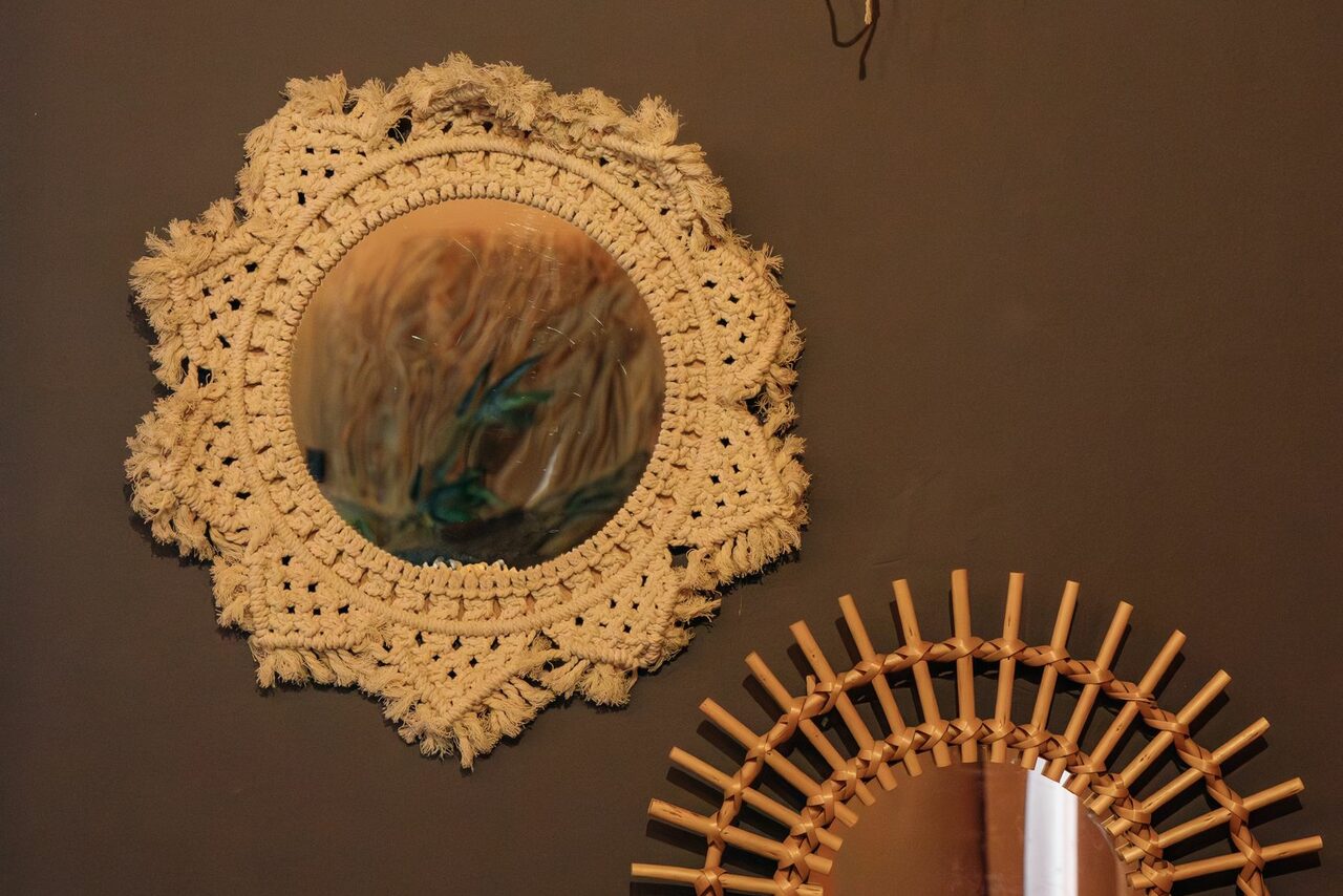 Арендовать Зал Ямайка. Лофт с большим диваном и экраном. Круглые зеркала на стене, одно в плетеной раме из веревок кремового цвета, другое с рамой из деревянных прутьев. Стена темно-серого цвета.