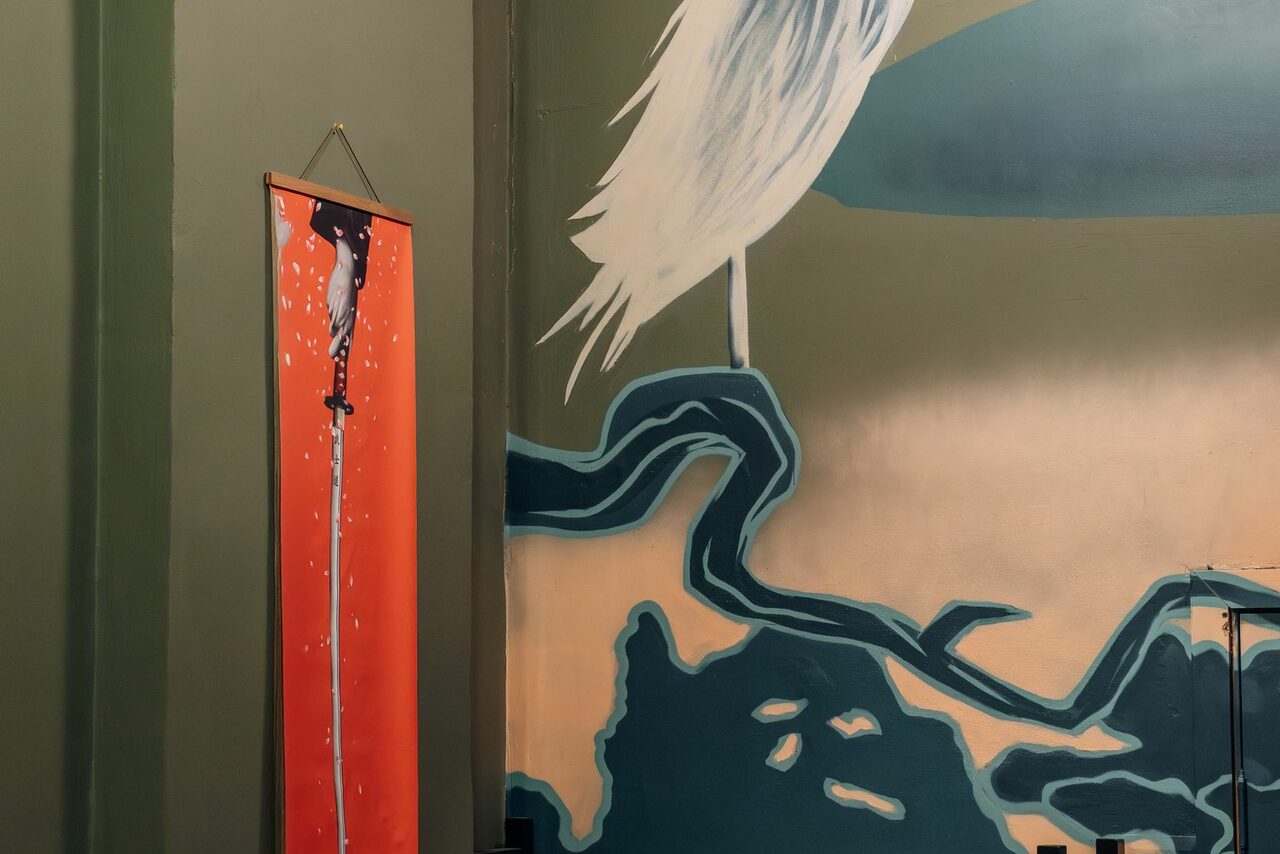 Арендовать Зал Китай. Лофт-зал в китайском стиле . Стена с художественной росписью: изображение белой птицы и абстрактные формы на зелёном фоне. Справа вертикальный красный баннер с черной фигурой и белыми каплями. Зеленый фон стены, смежные плоскости.