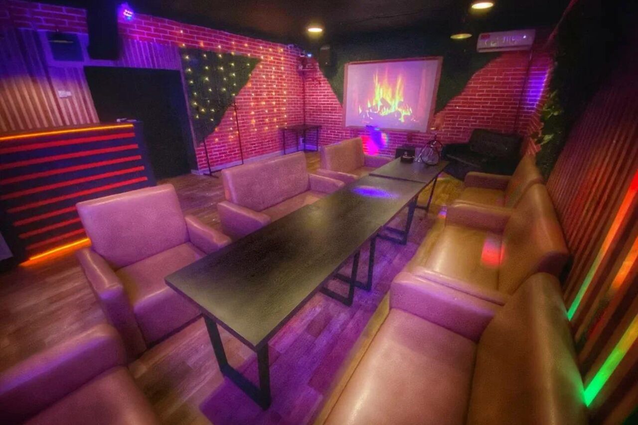 Арендовать Forest(Лес). Кирпичные стены, мягкие коричневые диваны и кресла, длинный черный стол. На стене проектор с изображением камина. Цветная подсветка и декоративные лампочки. Темное деревянное покрытие пола.