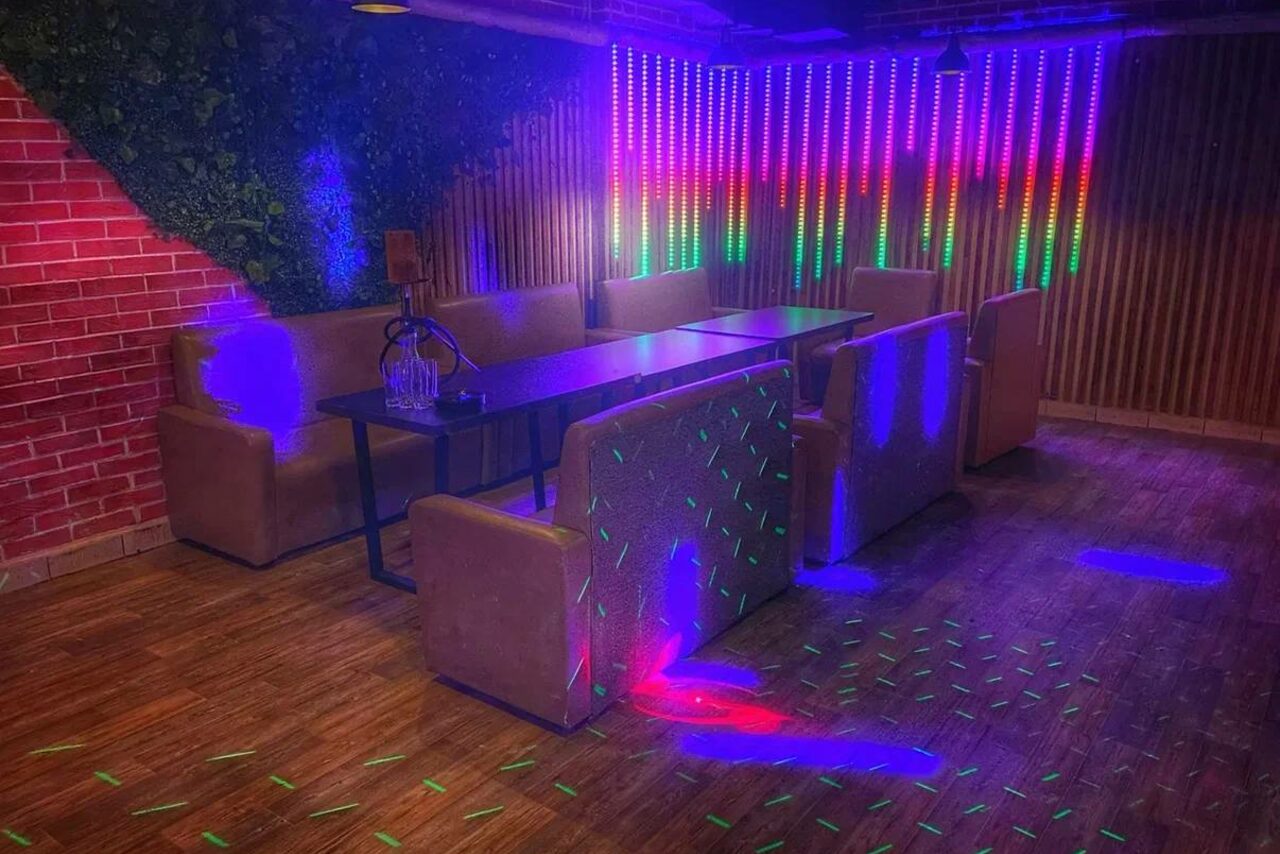 Арендовать Forest(Лес). Пространство для отдыха с диванами и столами, отделанное кирпичом и деревянными панелями. На стенах светодиодные полосы с меняющимся цветом освещения. Пол из дерева, декоративная зелень на стенах. Мягкая мебель коричневого цвета.