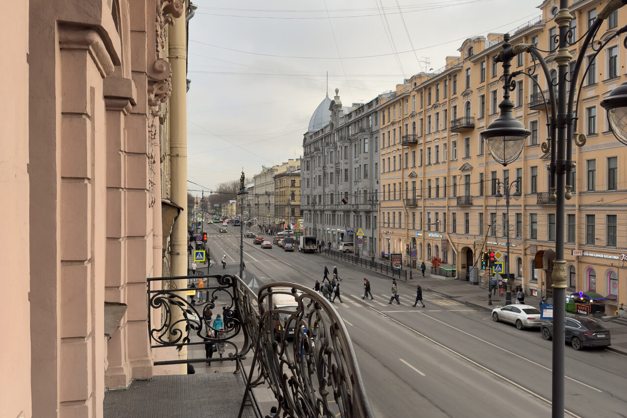 Арендовать Bedford studio (Бедфорд Студия). Объединённые светлые залы. Вид на городскую улицу с балкона. На переднем плане изящные кованые перила. Улица с автомобильным и пешеходным движением, вдоль нее расположены многоэтажные исторические здания пастельных тонов. Светлый дневной свет, уличные фонари.