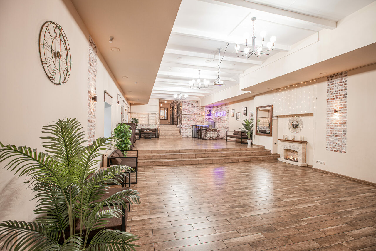 Арендовать Loft Lodge (Лофт Лодж) 7. Просторный уютный лофт. Просторное помещение с паркетным полом; зона с возвышением, украшенная кирпичной стеной; интерьер в светлых кремовых и кирпичных тонах; декоративные растения, металлические часы на стене, люстры на потолке, настенные картины и небольшая имитация камина.