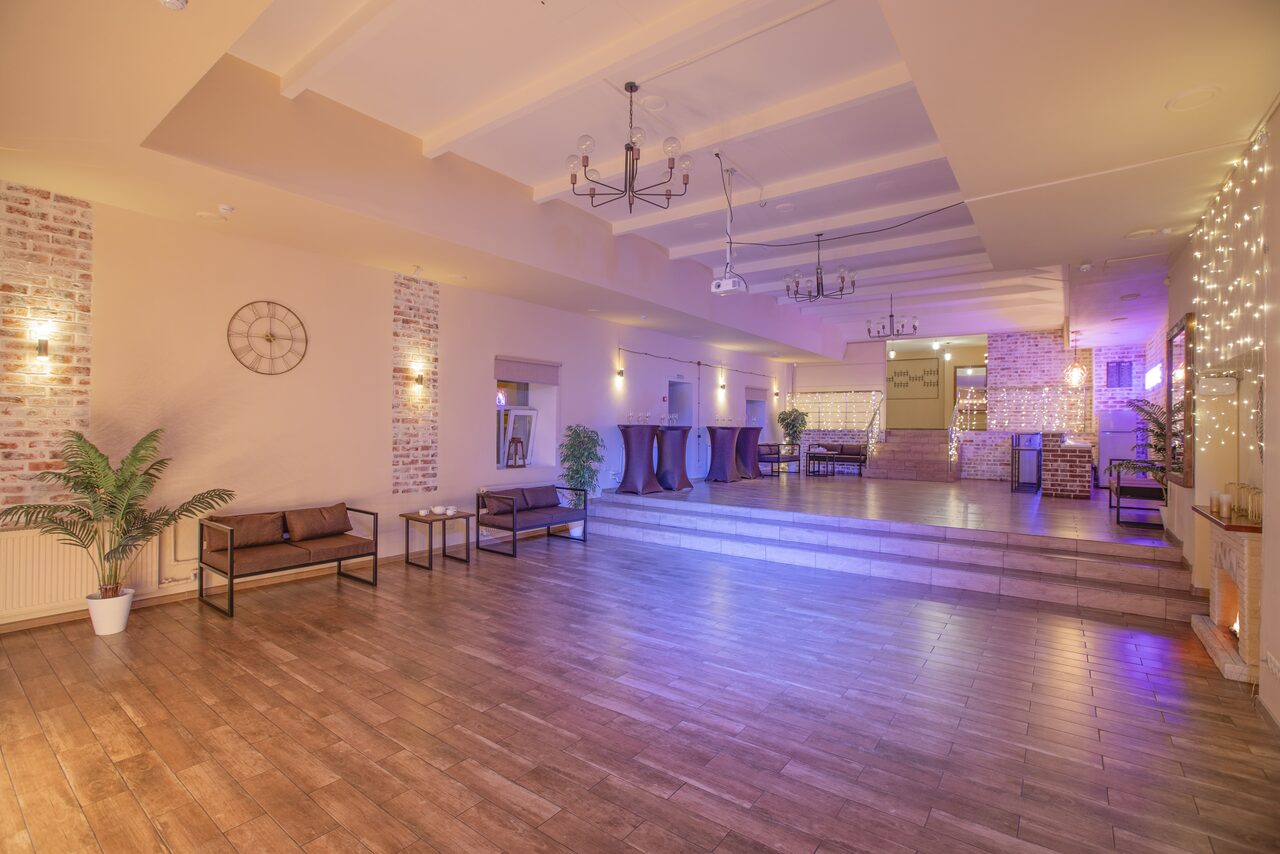 Арендовать Loft Lodge (Лофт Лодж) 7. Просторный уютный лофт. Просторное помещение с деревянным полом, декорированное светлыми стенами и кирпичной кладкой. На переднем плане стоят диваны и столики, на заднем - барные столы и стулья. Потолок со светильниками и люстрами, стены украшены гирляндами.