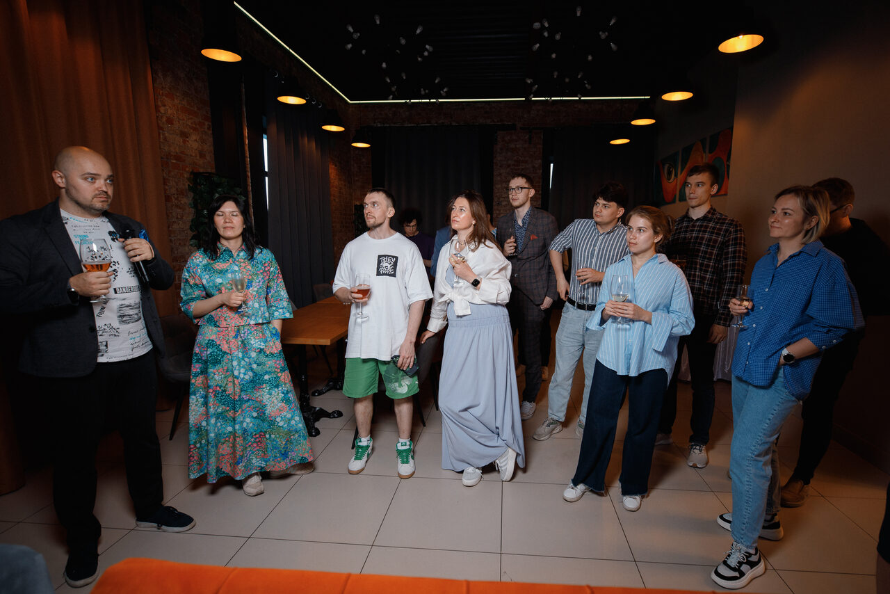 Арендовать Просторный лофт с видом на набережную. Пространство со светлыми плиточными полами и кирпичными стенами. Люди стоят с напитками. Мебель: стол, стулья. Освещение: подвесные круглые светильники. Цвета: оранжевый, синий, белый, зелёный. Тёмные шторы и декор на стене.