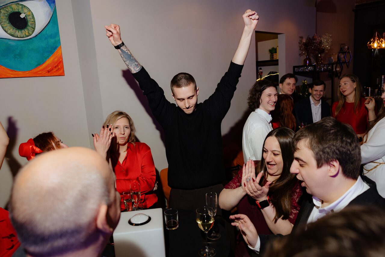 Арендовать Просторный лофт с видом на набережную. Внутреннее пространство с людьми, барная стойка или стол, пара бокалов на столе, нейтральные стены, цветное настенное искусство, подвесное освещение, деревянные элементы декора, люди сидят и стоят, многие в формальной одежде, гостеприимная атмосфера.