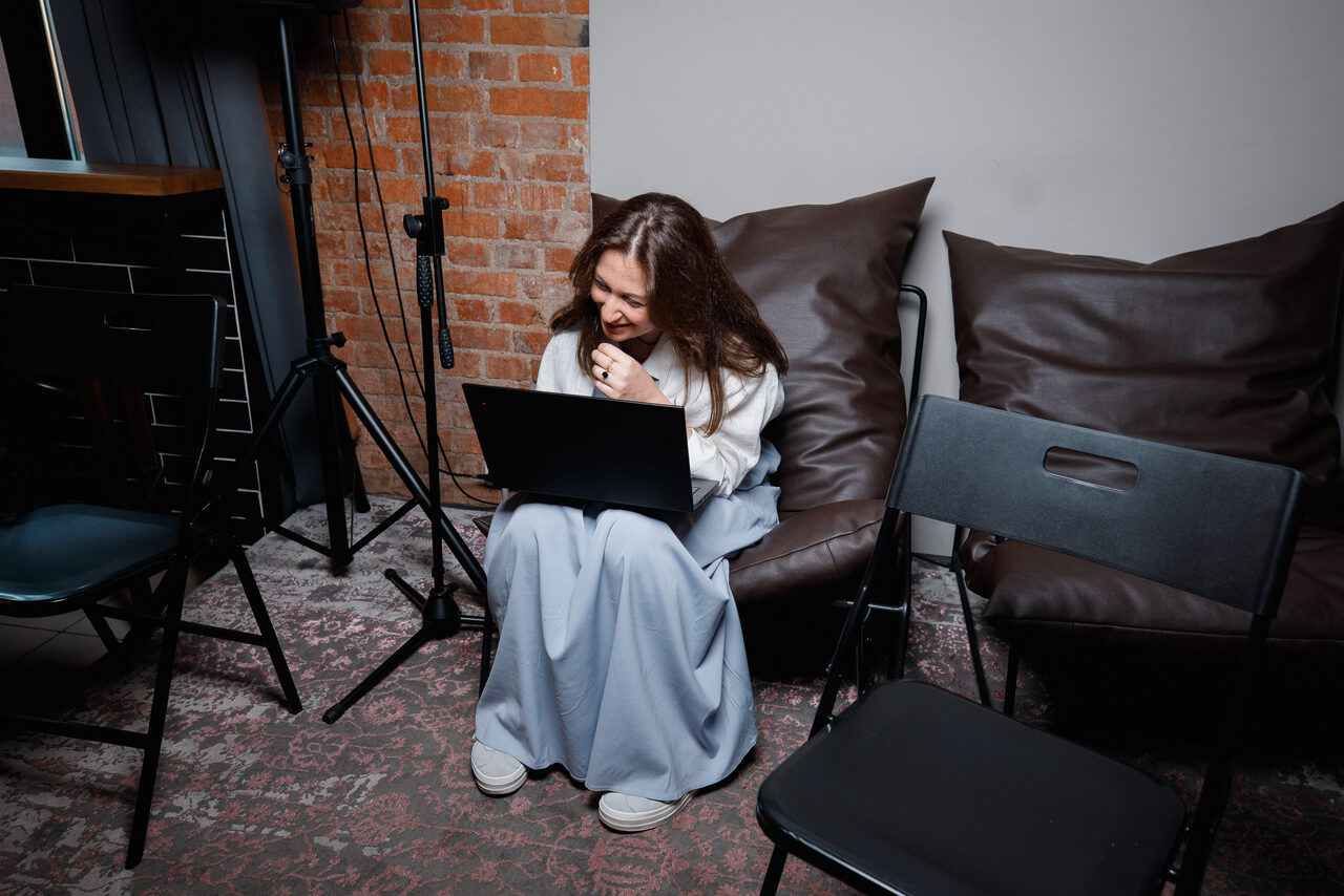 Арендовать Просторный лофт с видом на набережную. Пространство с кирпичной стеной и серой стеной, стулья из черного пластика и металла, два коричневых кресла-мешка, ковровое покрытие со сложным узором, искусственное освещение от лампы-стойки, написей и знаков нет.