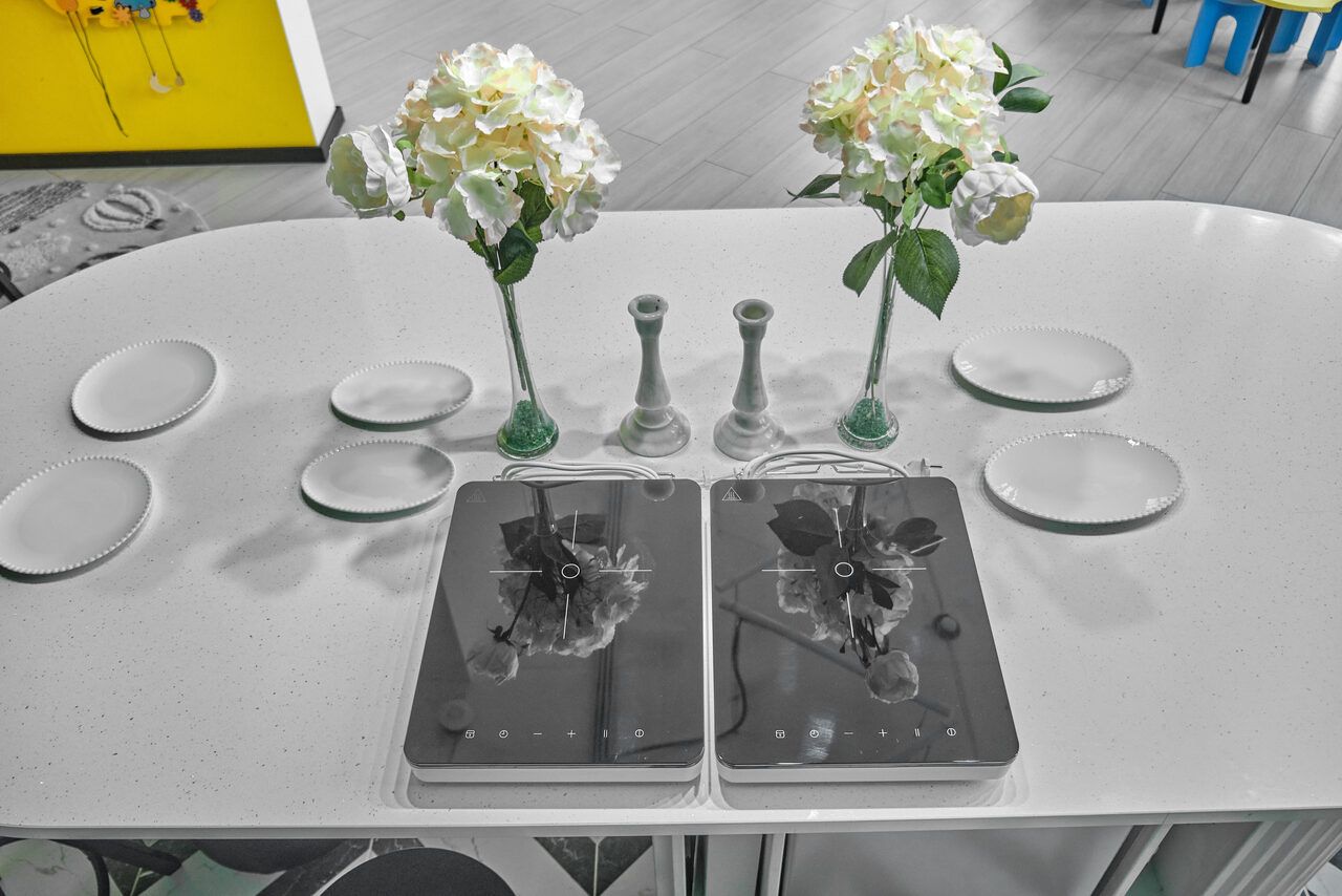 Арендовать Arcobaleno Loft(Аркобалено Лофт). Овальный белый стол с двумя белыми вазами с цветами, двумя белыми подсвечниками и шестью белыми тарелками. На столе расположены два планшета с отражением цветов. Фон яркий, с желтой и синей деталями. Светлое помещение.
