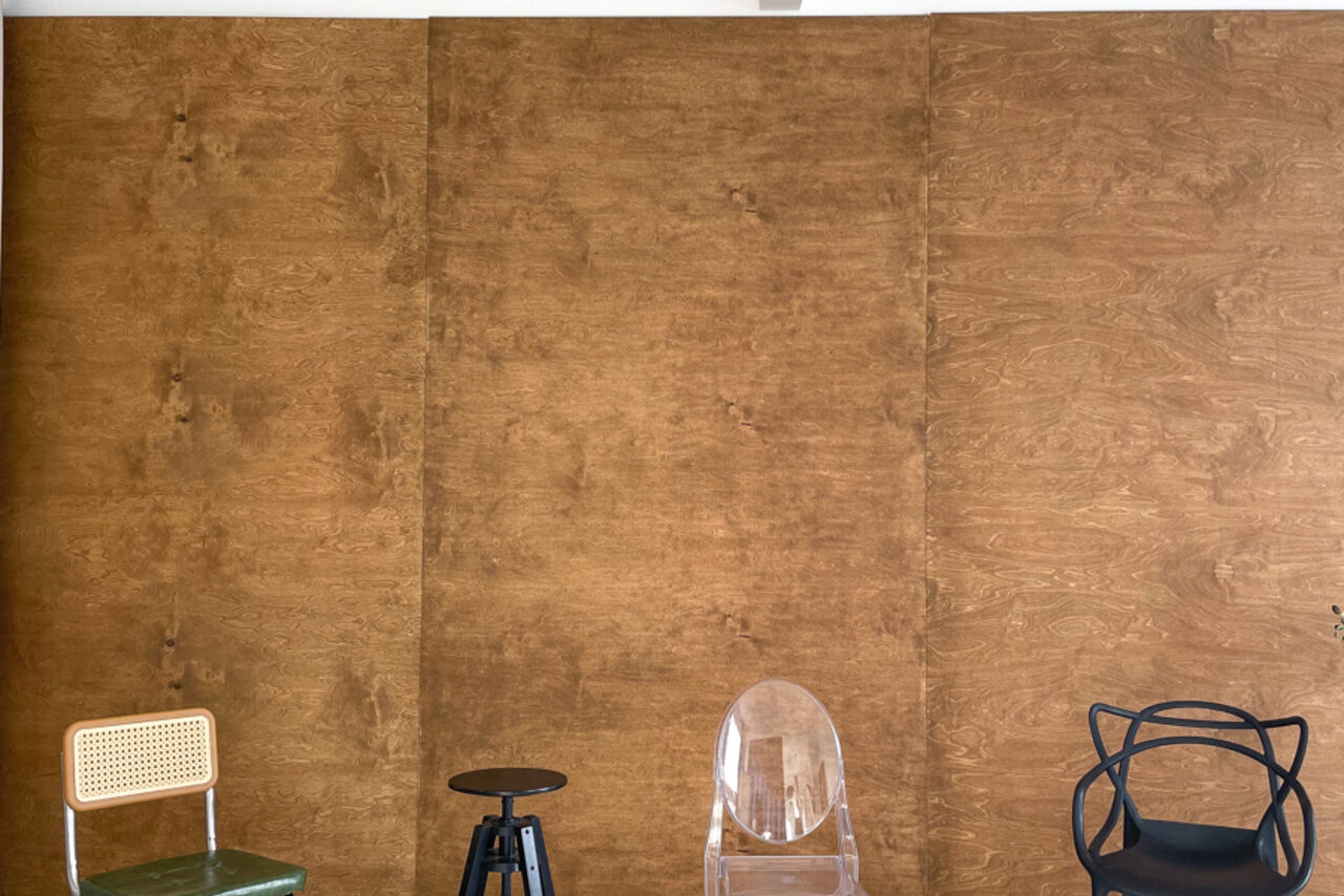 Арендовать Зал Серебро. Просторная и светлая фотостудия. Пространство с коричневыми деревянными стенами, включает различные стулья: прозрачный, чёрный с переплетением и бежевый из дерева и металла. Черный табурет. Настенное освещение отсутствует. Состояние мебели хорошее.