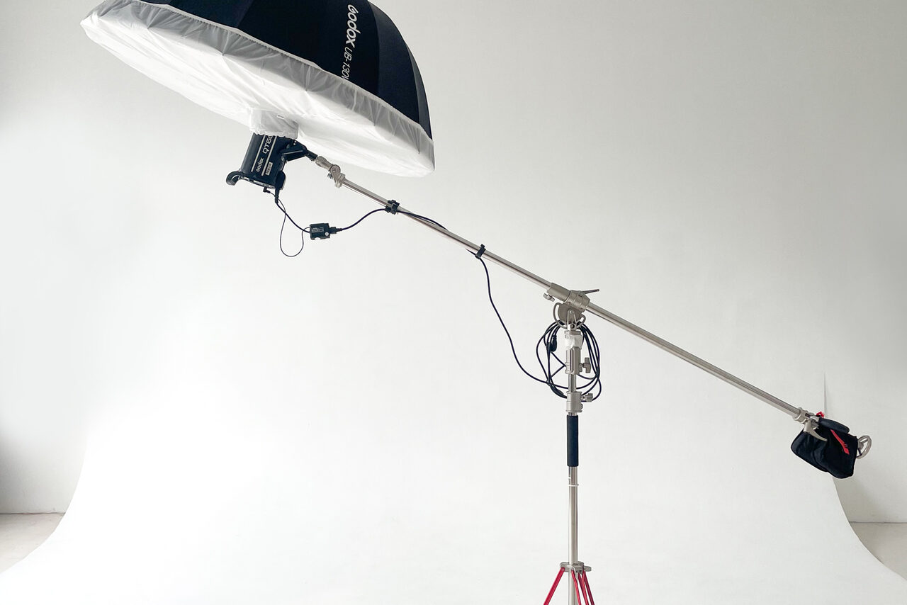 Арендовать Зал Серебро. Просторная и светлая фотостудия. Студийное пространство с белым циклом; осветительное оборудование на стойке с зонтом для рассеивания света; металлоконструкция, провода, белые стены и пол, плавный переход между стенами и полом, кранштейн на стойке.