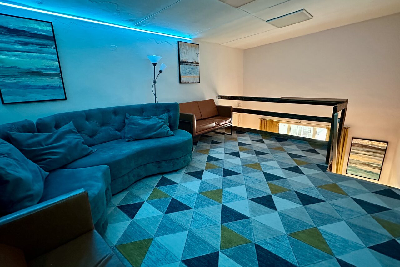 Арендовать Яркий двухуровневый лофт. Второй этаж лофта. Голубое освещение. Угловой диван. На стенах картины