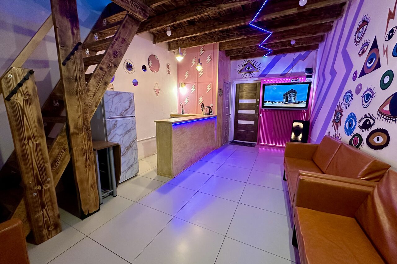 Арендовать Яркий двухуровневый лофт. Барная стойка. Холодильник. Разноцветные украшенные стены. Диваны. Телевизор. Лестница на второй этаж