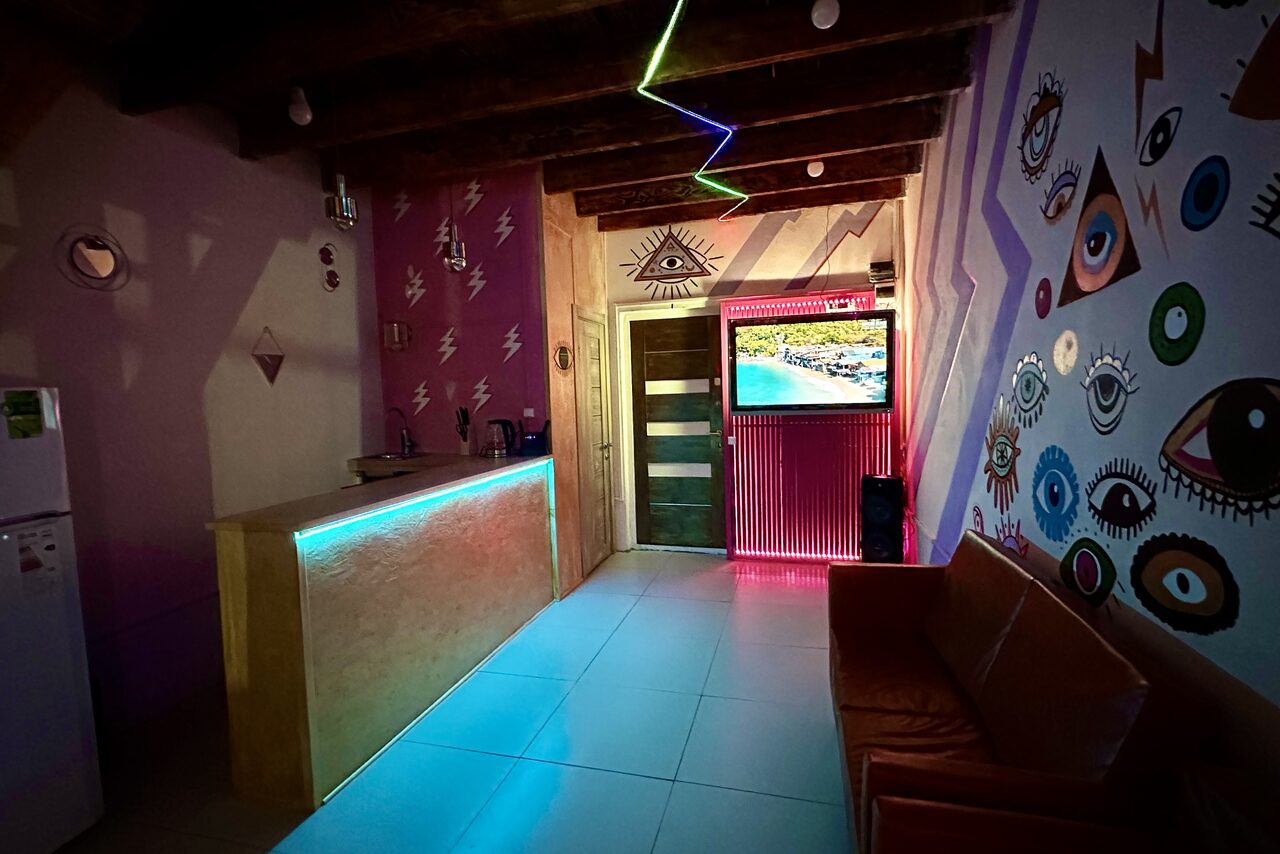 Арендовать Яркий двухуровневый лофт. Приглушённый свет. Неоновая подсветка. Барная стойка. Холодильник. Разноцветные украшенные стены. Диваны. Телевизор. Лестница на второй этаж