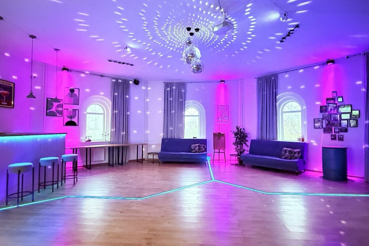 Арендовать Центрум. Уютное светлое пространство круглой формы. Просторное помещение с деревянным полом и несколькими арочными окнами, обставленное серыми диванами и барной стойкой с высокими стульями. Разноцветное подсвечивание, зеркальные шары на потолке, декоративные растения и фоторамки на стене.