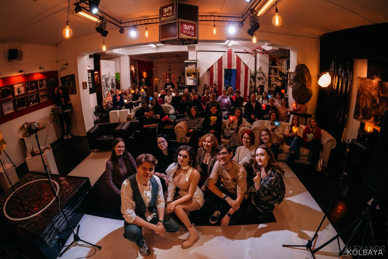 Арендовать А53: Secret Gallery (Секретная галерея). Просторное помещение с низким потолком и мягким освещением. В центре группа людей, сзади зрительный зал с сидящими людьми. Мебель: диваны и стулья. Декор: картины на стенах. Освещение: подвесные лампы. На полу черно-белое покрытие.