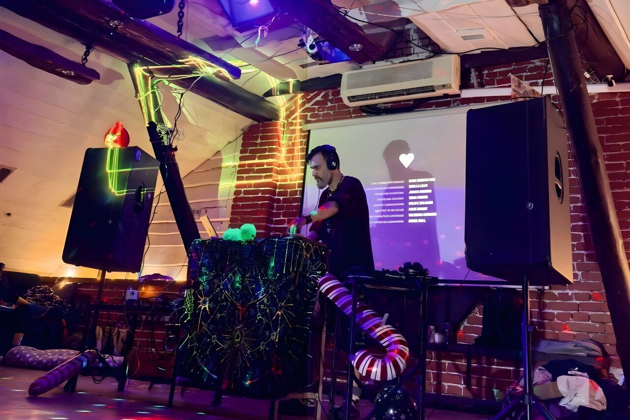 Арендовать Лофт-мансарда . Лофт-пространство с кирпичными стенами, системой кондиционирования. В центре находится DJ за пультом с декоративной подсветкой. Справа и слева установлены большие колонки. На стене проекция с текстом и иконкой в форме сердца.