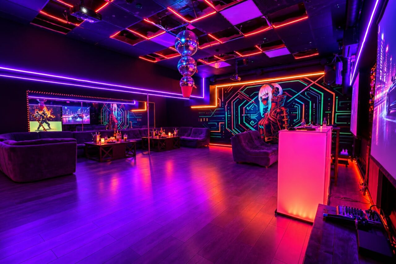 Арендовать Cyberpunk (Киберпанк). Клубное пространство с неоновым освещением, мягкой мебелью у стен, зеркалами, экраном, деревянным полом, столиками и баром. Декор в виде диско-шаров и графического настенного рисунка. Цвета: фиолетовый, розовый, синий.