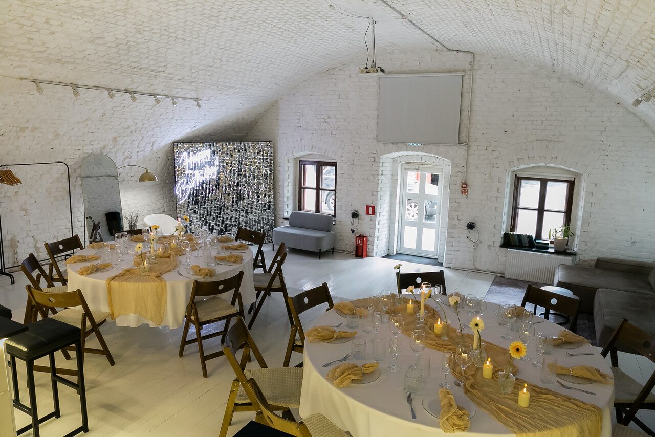 Арендовать Brodniki Loft (Бродники Лофт). Лофт из белого кирпича. Светлое помещение с белыми кирпичными стенами и сводчатым потолком. Расставлены круглые столы с белыми скатертями и деревянными стульями. На столах сервировка и цветы. Есть мягкая мебель, окна, проектор, и декоративные панели.
