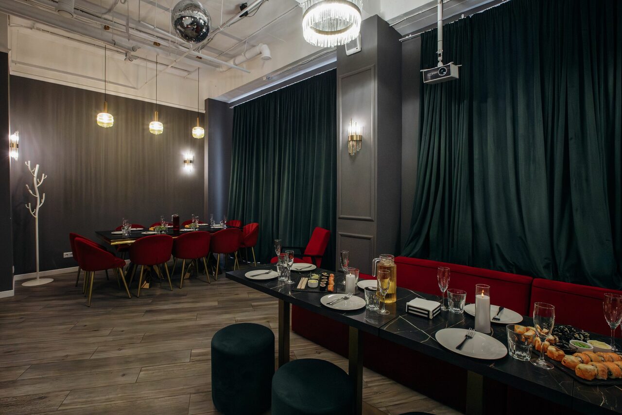 Арендовать Rubin Loft (Рубин Лофт). Лофт Вегас. Современное помещение с паркетным полом и высокими потолками. Столы с посудой и закусками, красные и зелёные стулья. Потолочные и настенные светильники. Тёмные шторы, серые стены. Декоративное зеркало-шар на потолке.