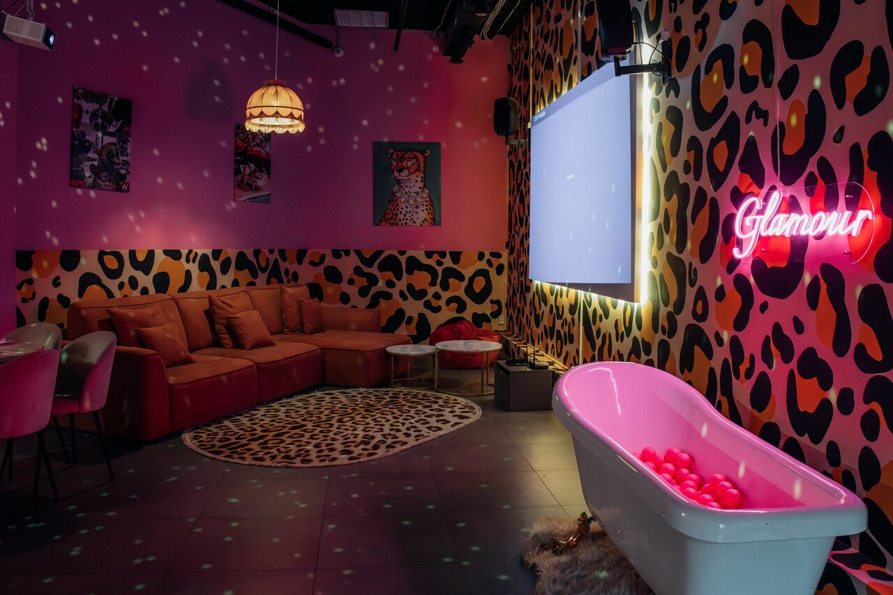 Арендовать Лофт Гламур. Лофт в стиле глэм с яркими леопардовыми узорами на стенах, розовыми и оранжевыми элементами. Угловой диван, столик, ванна с шарами, неоновый знак «Glamour». Настенные светильники, коврики, проектор или экран на стене.