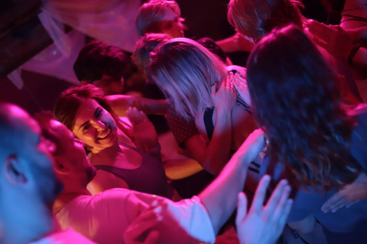 Арендовать Лес. Театральный лофт с верандой, сценой и вторым ярусом. Группа людей тесно взаимодействует в помещении с приглушенным освещением, преобладают розовые и фиолетовые оттенки. Видно, что они одеты в повседневную одежду. На заднем плане тканевые драпировки.