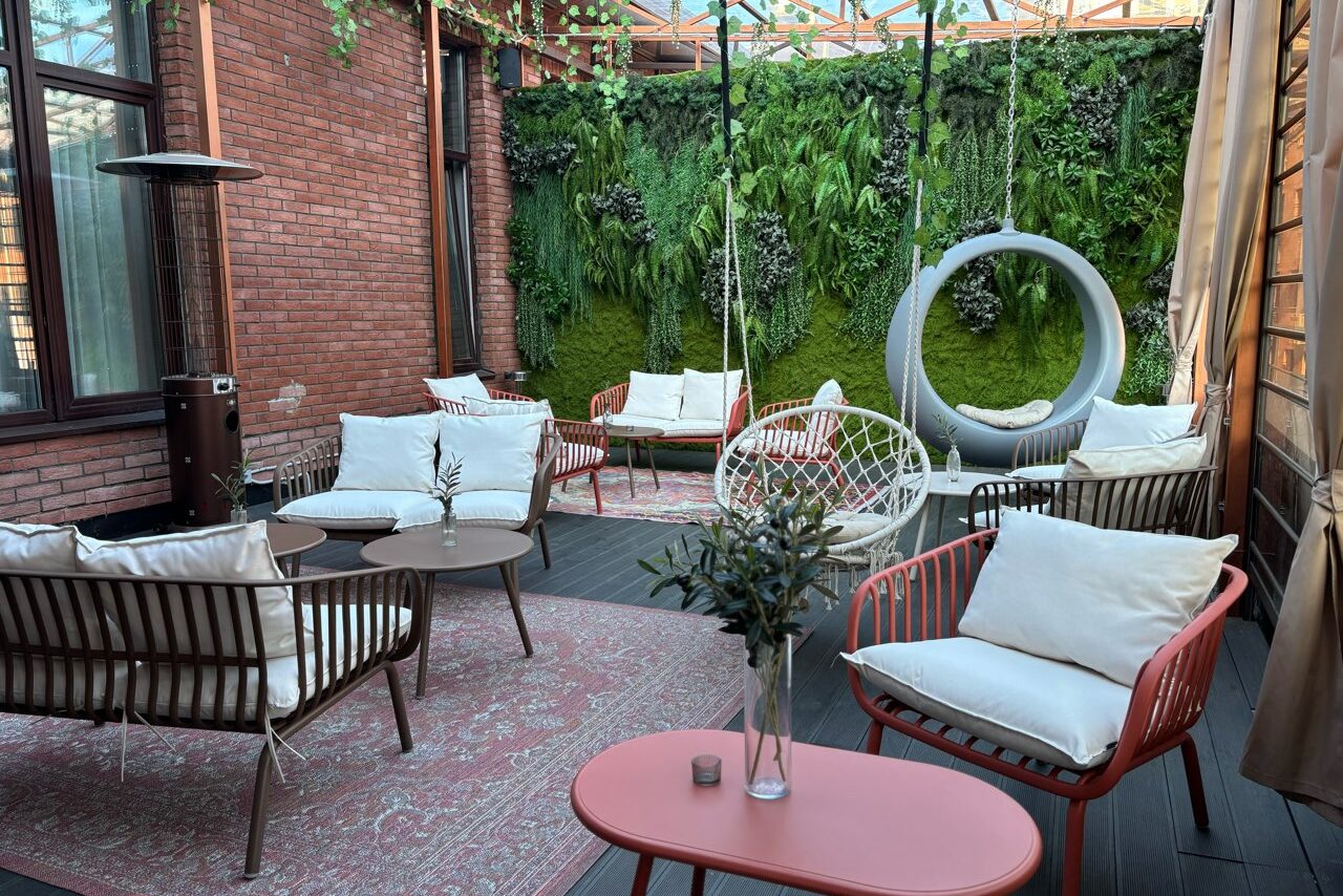 Арендовать Лофт Loftsinoby (Лофтсиноби)  для мероприятий. Частично крытое пространство с деревянными полами и кирпичными стенами. Мебель: кресла и диваны с подушками, подвесное круглое кресло. Зеленая стена с растениями, круглые деревянные столы. Освещение естественное, через стеклянную крышу.