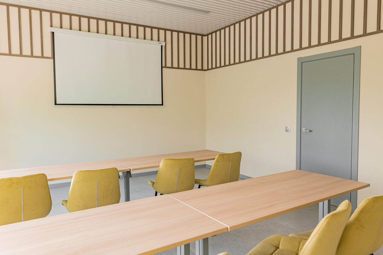 Арендовать Зал 5. Светлый малый конференц-зал до 20 человек в Академии Кантаты. Просторное помещение с бежевыми стенами; серый дверной проем. Продолговатые светлые деревянные столы, вокруг которых расположены желтые стулья на колесиках. На стене установлен белый экран для проекции. Потолок оформлен светлыми панелями и деревянными рейками.