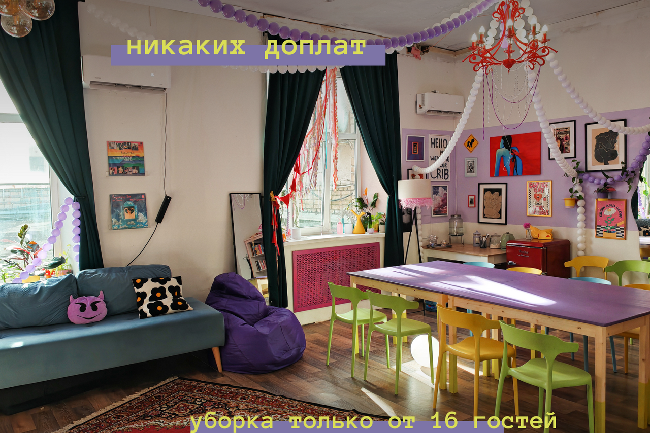 Арендовать Дофаминовый лофт для девичиков, мастер-классов и других уютных встреч. Гостиная с большим обеденным столом, фиолетовыми и зелеными стульями, синим диваном и фиолетовым креслом-мешком. На белых стенах картины и плакаты. Красная люстра, темные шторы. Надписи: “никаких доплат”, “уборка только от 16 гостей”.