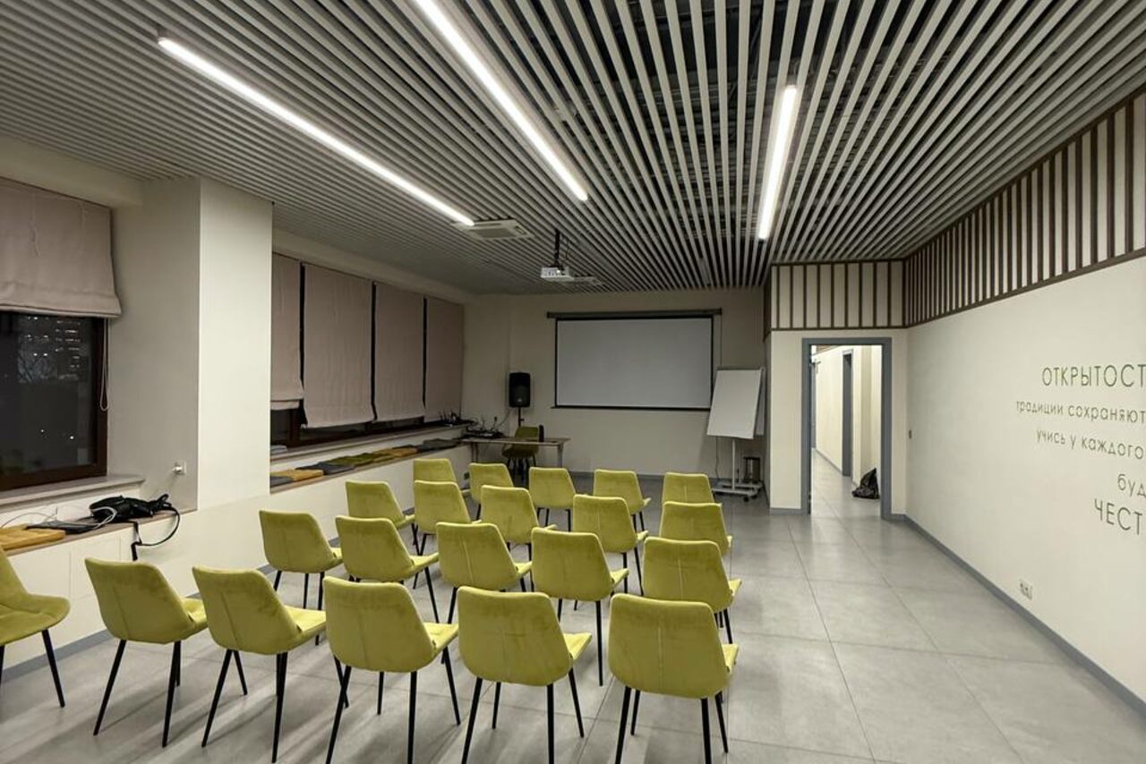 Арендовать Зал 6. Просторный и светлый конференц-зал до 50 человек в Академии Кантаты. Просторное помещение с проектором и экраном, светло-зелёные стулья в несколько рядов, светло-серые плиточные полы, подвесной белый потолок с ламелями, белые стены с текстом. Настенные светильники, флипчарт у стены.