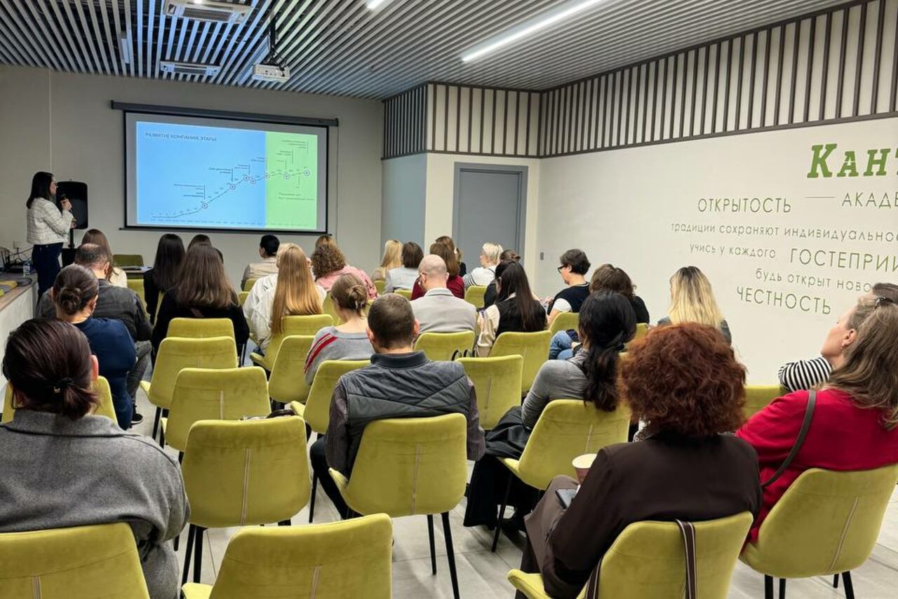 Арендовать Зал 6. Просторный и светлый конференц-зал до 50 человек в Академии Кантаты. Конференц-зал с рядами желтых кресел, люди сидят и смотрят на экран с презентацией. Потолок с линейными светильниками, стены белые с надписями. Справа текст на русском языке о честности и этике.