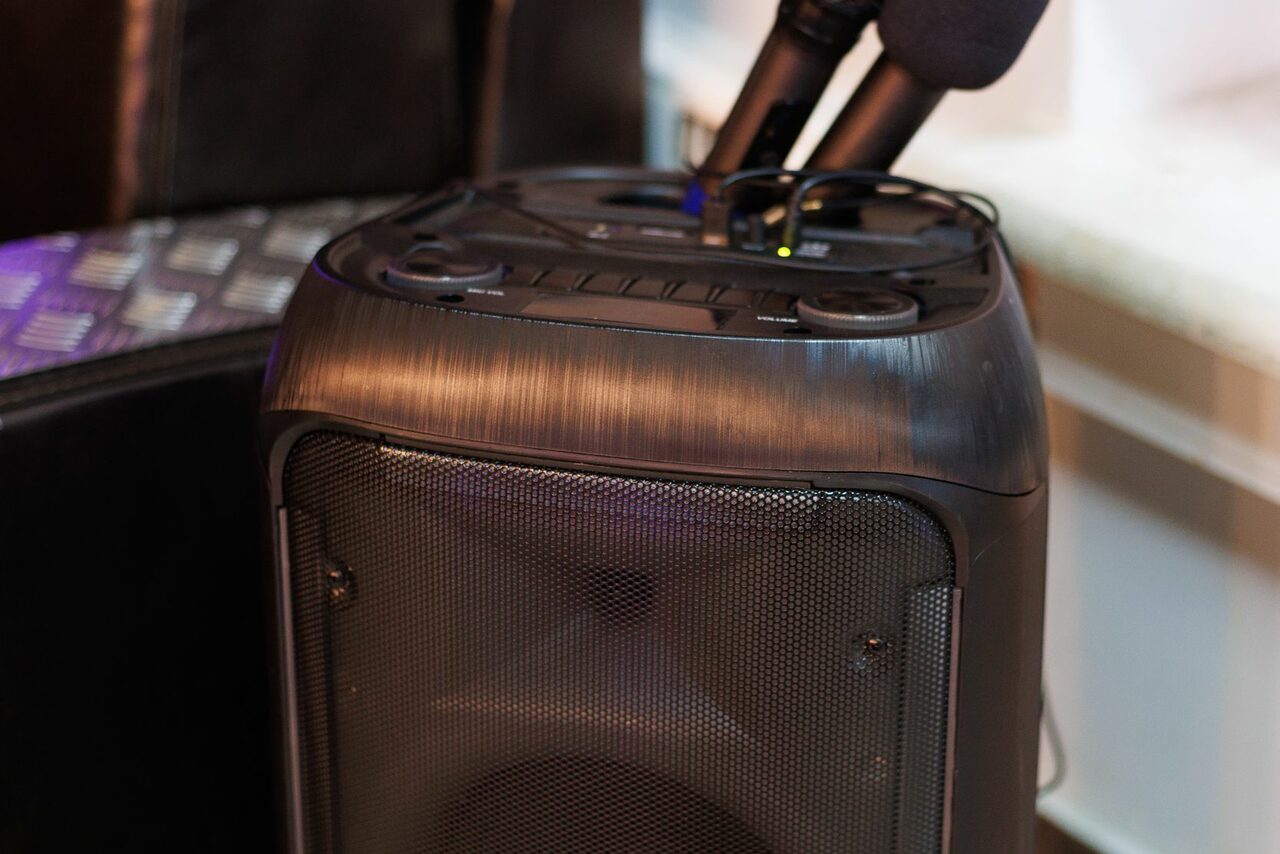 Арендовать Лофт Семеновский. Портативная аудиосистема черного цвета с двумя микрофонами на верхней панели, расположенная на фоне металлической поверхности и светло-бежевой стены.