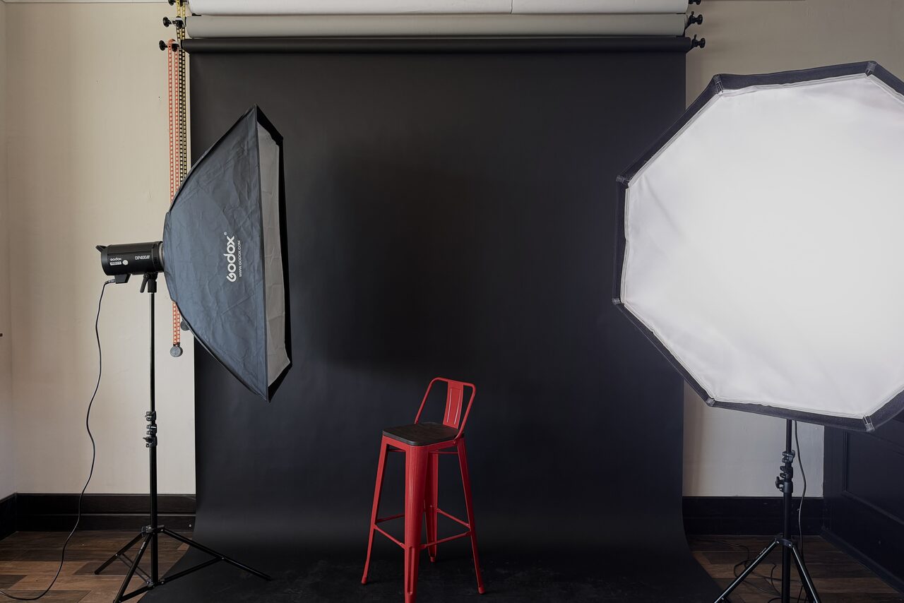 Арендовать Студия Н. Фотостудия с черным фоном, двумя софтбоксами на стойках и высоким красным стулом. Стена светлая, пол из темного дерева.