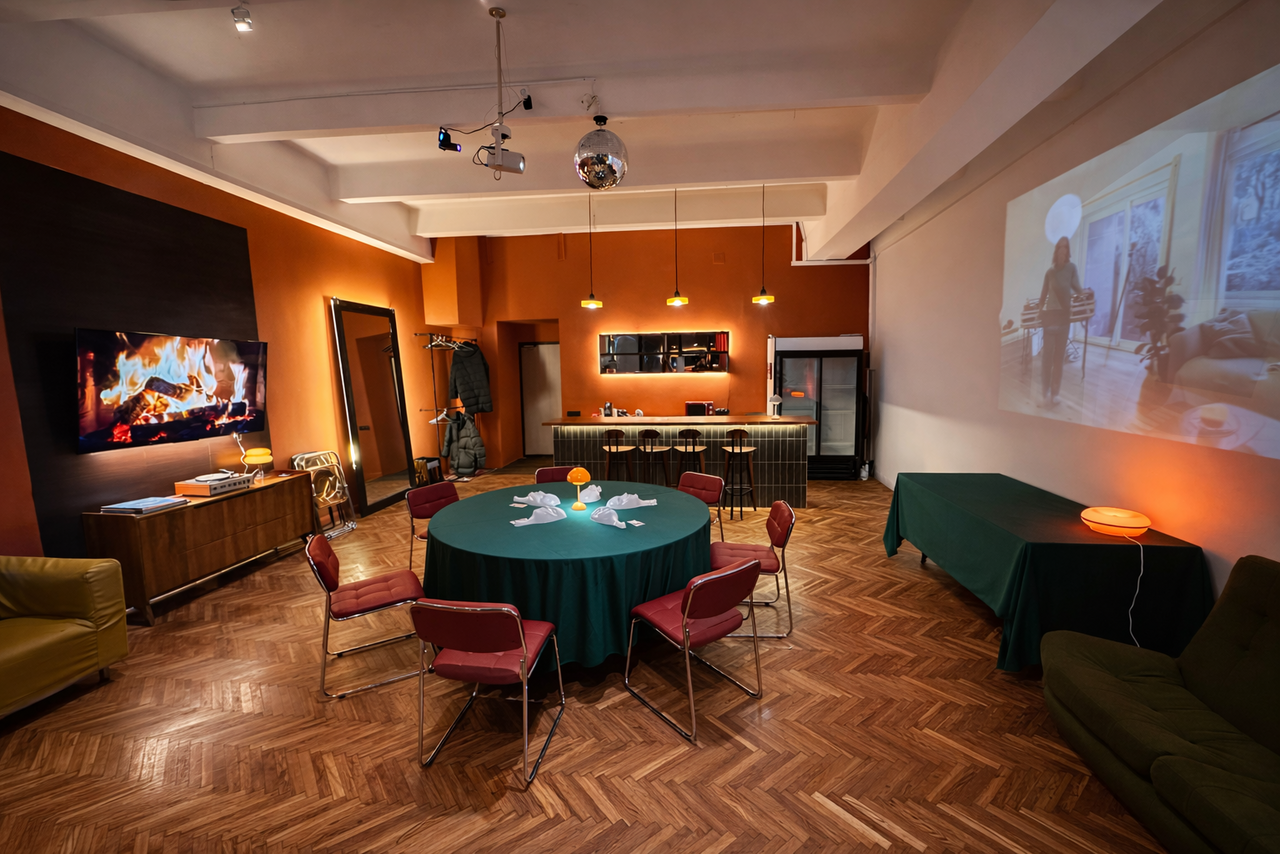 Арендовать The Gallery Loft (Лофт Галерея) . Просторное помещение с деревянным паркетом, круглый стол с зелёной скатертью и стульями, барная стойка, холодильник, диваны, проектор на стене, декоративный камин. Освещение: потолочные светильники и бра. Декор: зеркало, картина, растения.