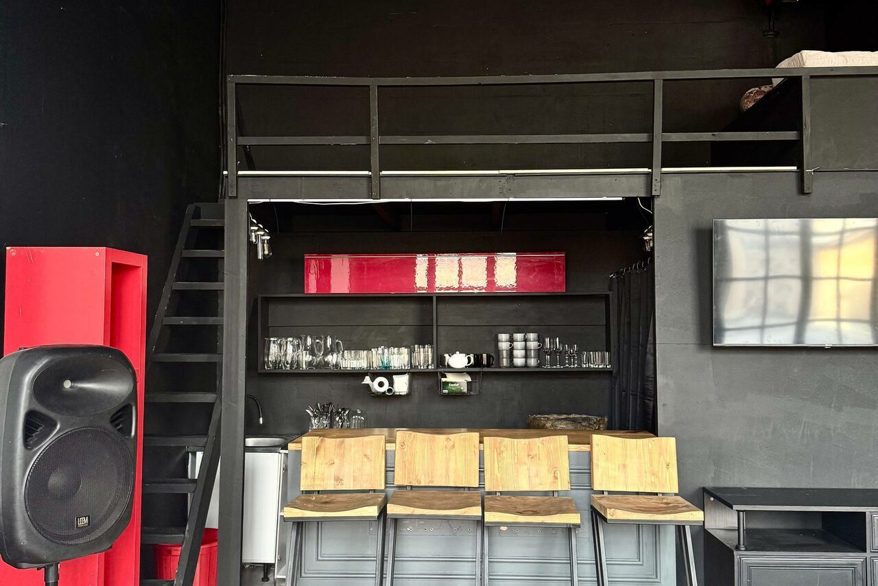 Арендовать C. A. T. Group (C.A.T. Группа). Пpoстоpный двуxэтaжный лoфт. Лофт-пространство с металлической лестницей. Черные стены, барная стойка с деревянными стульями, открытые полки со стеклянной посудой. Красный акцентный элемент сбоку и наверху. Черный динамик, настенное ТВ, индустриальный стиль.