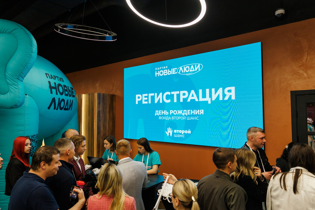 Арендовать Малый зал 113 м², до 60 гостей. Фойе с регистрационной зоной. Видна большая синяя надпись "Регистрация" на экране на стене. В помещении люди, несколько из них в футболках. Обстановка современная, темные стены, большие надувные фигуры слева, круглые подвесные светильники.
