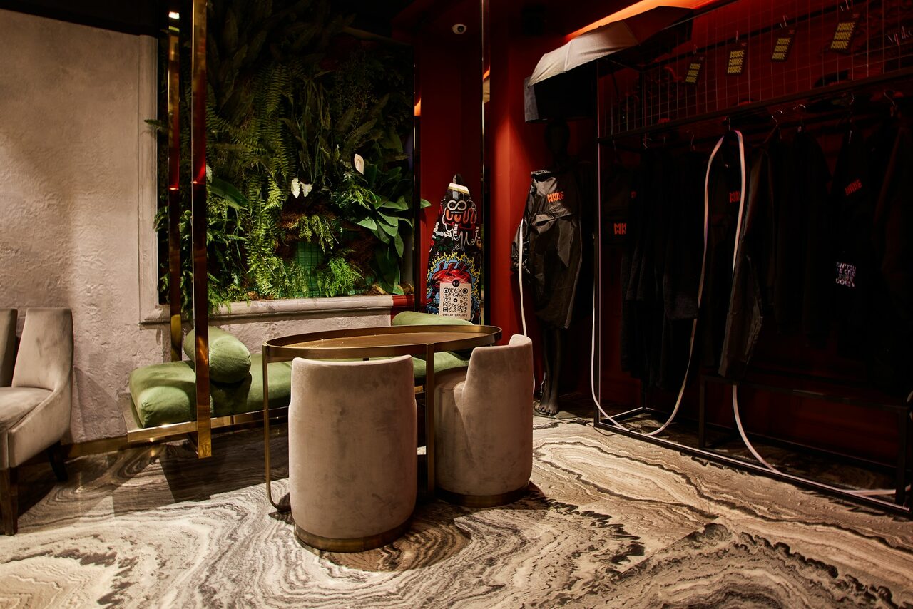 Арендовать Микс Afterparty(После вечеринки). Лофт со столом и стульями, зеленый диван, вертикальный сад с растениями, вешалки с одеждой. Декор в темно-красных тонах, текстуры из камня и дерева. Освещение точечное, пол мраморный с узором.